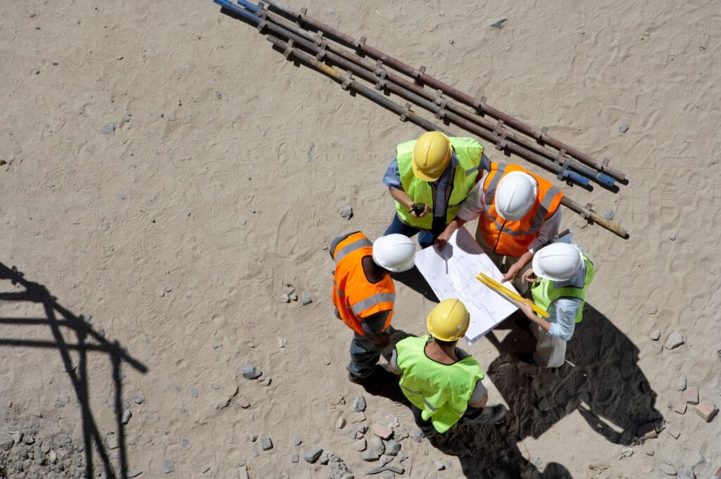 Demolition crew in PPE hard hats and reflective vests are meeting to discuss a project blueprint