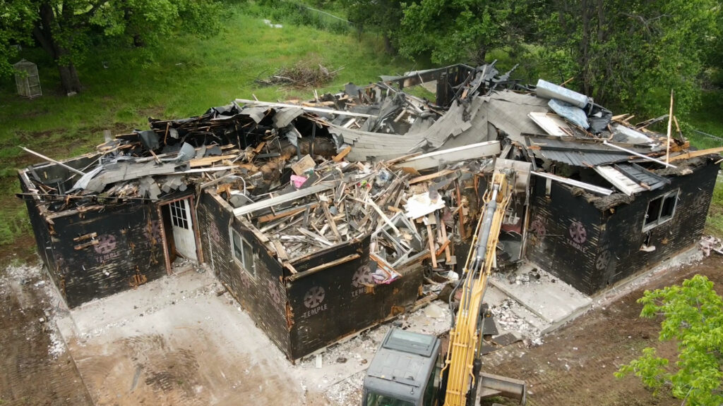 Midway through Wannco Services home demolition project in Granbury, TX for a home destroyed by a house fire. An excavator is beginning to tear down the wood and walls after the brick material was removed for reuse. 