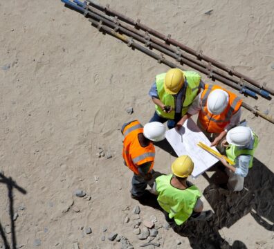 Demolition crew in PPE hard hats and reflective vests are meeting to discuss a project blueprint