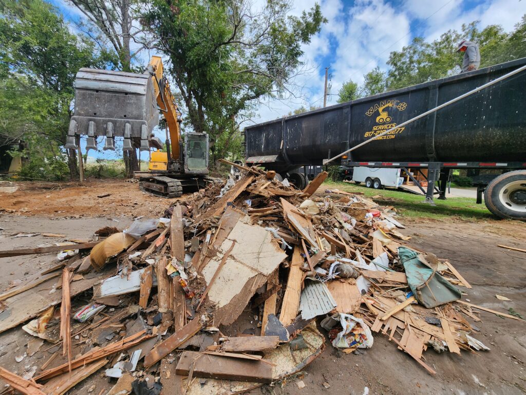 A Wannco excavator next to a pile of debris and a roll away dumpster after doing a demolition in Tolar