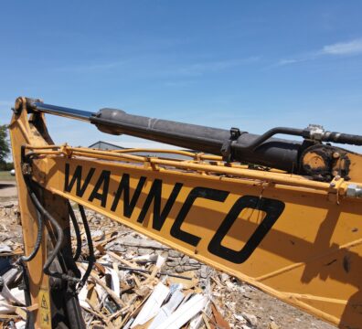 View of an excavator arm that says Wannco across it among a debris pile